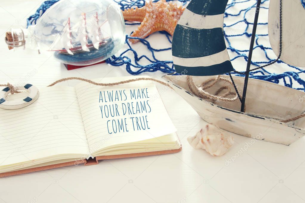 nautical concept image with white decorative sail boat and notebook: ALWAYS MAKE YOUR DREAMS COME TRUE.