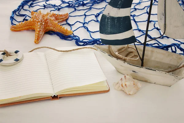Nautiska konceptet bild med vita dekorativa segelbåt och Tom öppna anteckningsboken över vitt trä bord. — Stockfoto