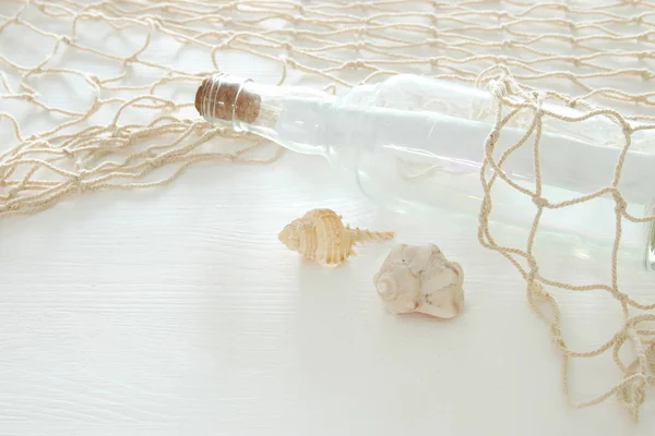 Nautische concept afbeelding met letter in de fles, schelpen en vissen net over witte houten tafel. — Stockfoto