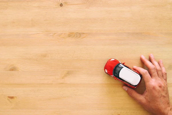 Top view photo of man's hand holding toy car over wooden background. — Stock Photo, Image