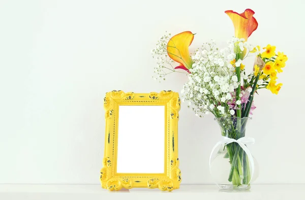 Immagine di un bellissimo mazzo di fiori gialli primaverili accanto a una cornice bianca vintage su un tavolo bianco. Per la fotografia fingere montaggio . — Foto Stock