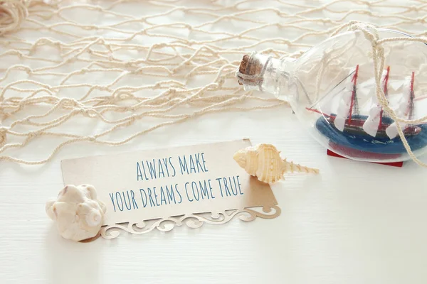 Nautical concept image with sail boat in the bottle and note: ALWAYS MAKE YOUR DREAMS COME TRUE. — Stock Photo, Image
