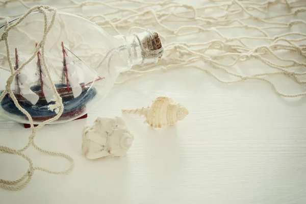 白の木製テーブルの上の瓶の中の白い網タイツ、貝殻と帆ボートで航海のコンセプト イメージ. — ストック写真