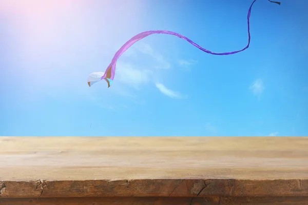 Imagen de una mesa rústica vacía frente a una cometa colorida volando en el cielo azul a través de las nubes. Para la presentación del producto . — Foto de Stock