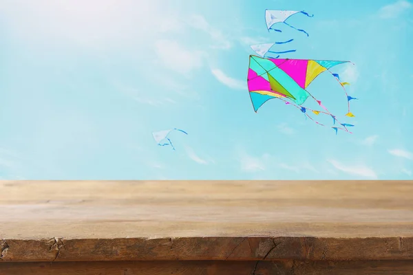 Image d'une table rustique vide devant un cerf-volant coloré volant dans le ciel bleu à travers les nuages. Pour la présentation du produit . — Photo