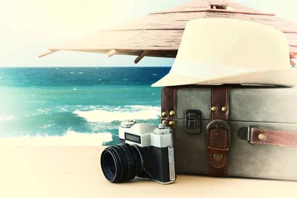 Reiziger vintage bagage, camera en fedora hoed over houten tafel infront van zee landschap. vakantie en vakantie concept. — Stockfoto