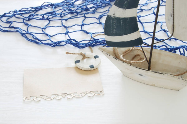nautical concept image with white decorative sail boat and note over white wooden table.