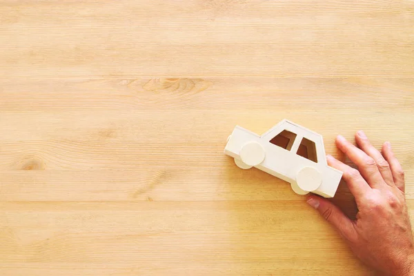 Top view photo of man's hand holding toy car over wooden background. — Stock Photo, Image