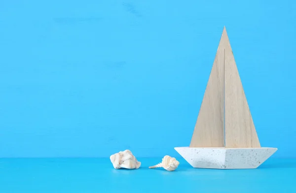 Морская концепция с белой декоративной парусной лодкой и ракушками на синем деревянном столе и фоне . — стоковое фото