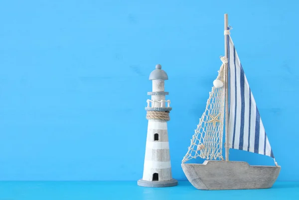Nautische concept met witte decoratieve zeilboot en vuurtoren over blauwe houten tafel en achtergrond. — Stockfoto