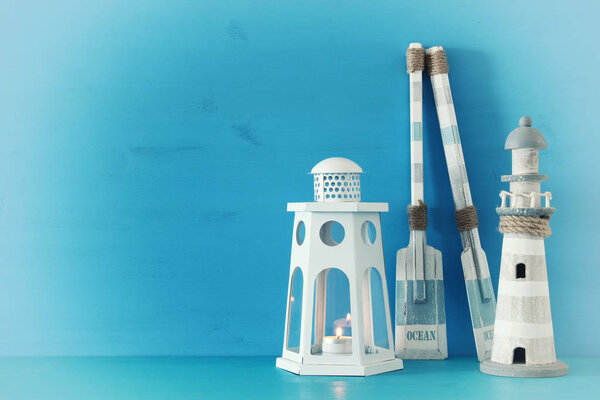 nautical concept with white decorative lantern, lighthouse and wooden boat oars over blue background.