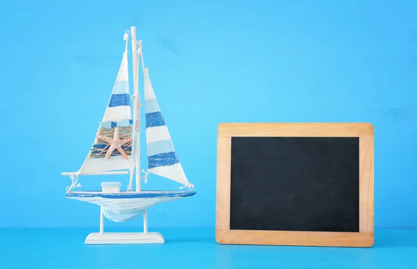 Nautische concept met witte decoratieve houten boot naast leeg schoolbord voor kopie ruimte over blauwe achtergrond. — Stockfoto