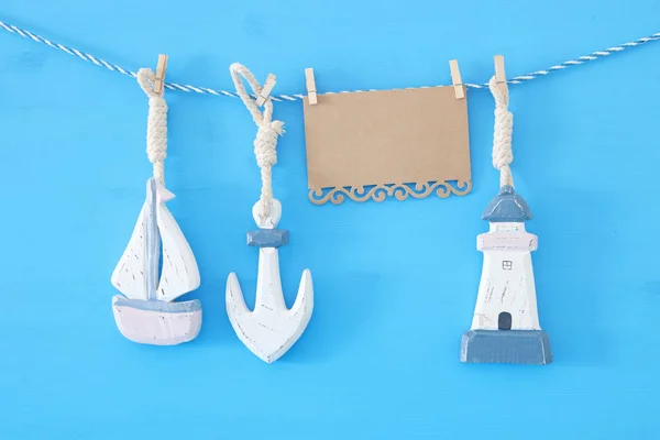 Nautical concept with sea lifestyle decorations: sail boat and anchor hanging on a string over blue wooden background. — Stock Photo, Image