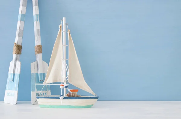Concetto nautico con barca a vela decorativa bianca e remi in legno su sfondo blu . — Foto Stock
