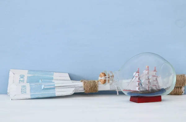 Concepto náutico con remos de madera y barco en la botella de vidrio sobre fondo azul . —  Fotos de Stock