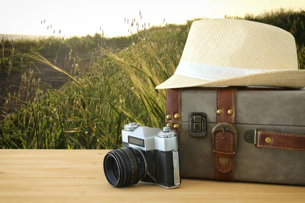Мандрівник старовинний багаж, камера і капелюх годівниці над дерев'яним столом на фоні поля під час заходу сонця. концепція відпочинку та відпустки . — стокове фото