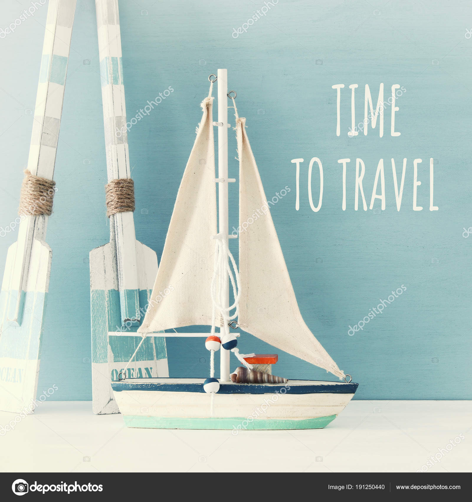 Nautical Concept With White Decorative Sail Boat And Wooden Oars Nautical Concept With White Decorative Sail Boat And Wooden Oars Over Blue Background Stock