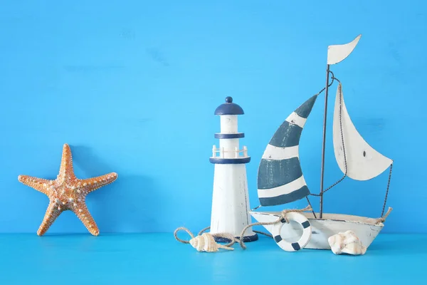 Nautische concept met witte decoratieve zeilboot, vuurtoren, zeesterren, schelpen over blauwe houten tafel en achtergrond. — Stockfoto