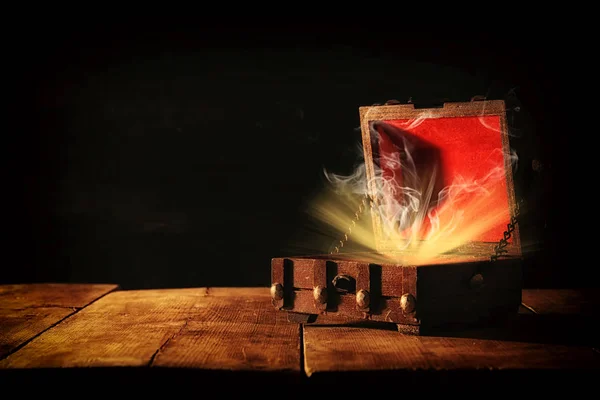 Bild einer geheimnisvollen Schatztruhe mit Licht und Rauch über einem alten Holztisch. — Stockfoto
