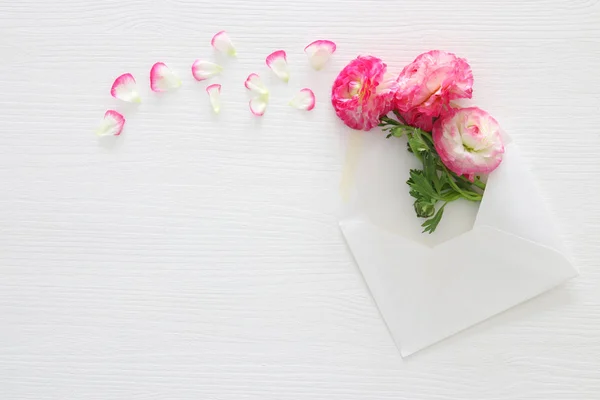 Image of envelope with delicate pastel pink beautiful flowers arrangement over white wooden background. Flat lay, top view. — Stock Photo, Image