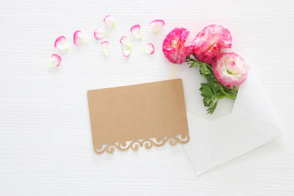 흰색 나무 배경 위에 섬세 한 파스텔 핑크 아름 다운 꽃 배열 가진 봉투의 이미지. 평면 위치, 최고 보기. — 스톡 사진