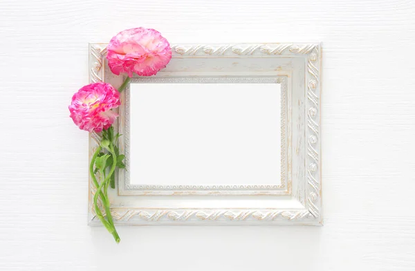 Image de délicat arrangement de belles fleurs rose pastel et cadre photo vintage vide sur fond blanc en bois. Couché à plat, vue de dessus. Pour la photographie montage maquette . — Photo