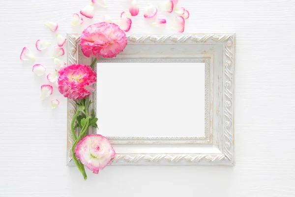 Imagen de delicada pastel rosa hermoso arreglo de flores y marco de fotos vintage vacío sobre fondo de madera blanca. Asiento plano, vista superior. Para montaje de maquetas fotográficas . — Foto de Stock