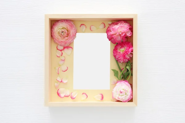 Imagen de delicada pastel rosa hermoso arreglo de flores y marco de fotos vintage vacío sobre fondo de madera blanca. Asiento plano, vista superior. Para montaje de maquetas fotográficas . — Foto de Stock