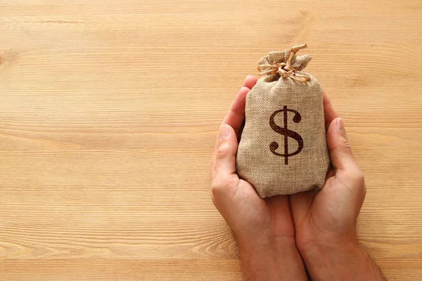 Mannelijke hand met een zak geld over houten bureau — Stockfoto