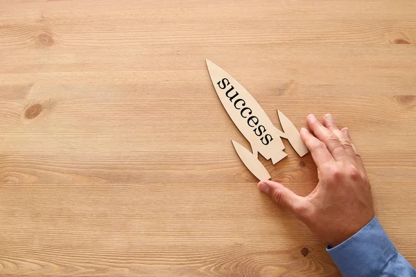 Mano del hombre sosteniendo cohete con la palabra - éxito - sobre fondo de madera . —  Fotos de Stock