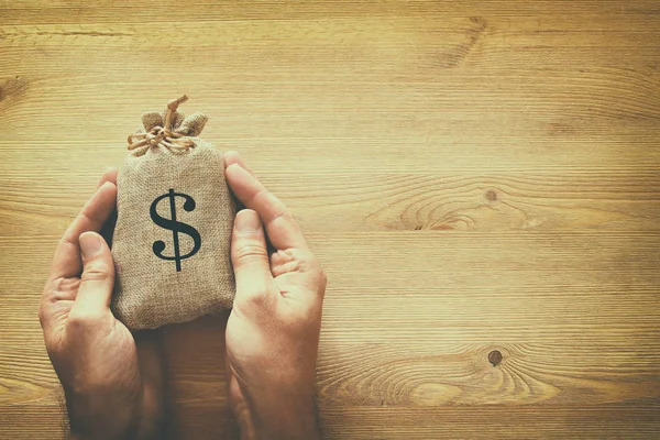 Mannelijke hand met een zak geld over houten bureau — Stockfoto