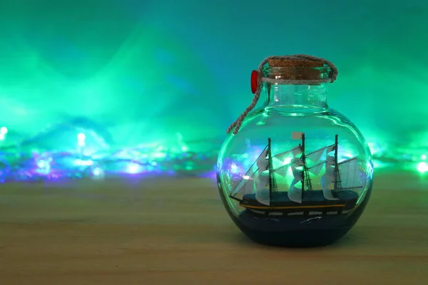 Image concept nautique avec voilier dans la bouteille et guirlande lumières sur table en bois. Concentration sélective . — Photo