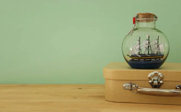 Морское концептуальное изображение с парусной лодкой в бутылке и старым чемоданом над деревянным столом. Селективный фокус . — стоковое фото
