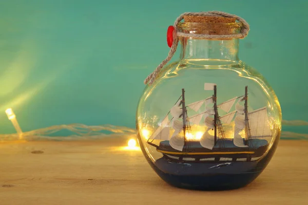Imagem conceito náutico com barco à vela na garrafa e luzes guirlanda de ouro sobre mesa de madeira. Foco seletivo . — Fotografia de Stock