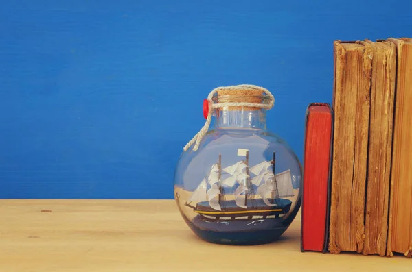 Nautisches Konzeptbild mit Segelboot in der Flasche neben alten Büchern über Holztisch. Selektiver Fokus. — Stockfoto