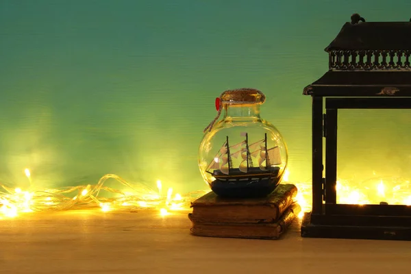 Nautical concept image with sail boat in the bottle next to old books over wooden table. Selective focus. — Stock Photo, Image