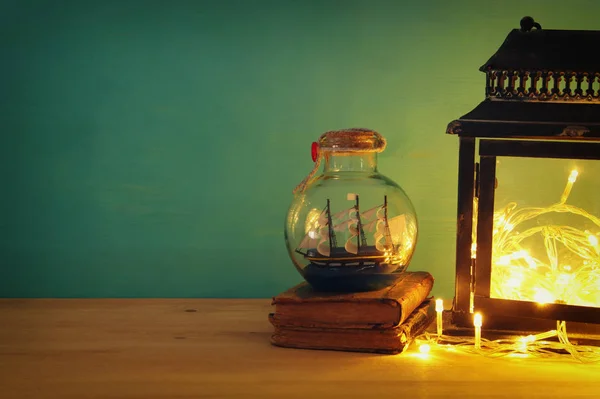 Nautical concept image with sail boat in the bottle next to old books over wooden table. Selective focus. — Stock Photo, Image