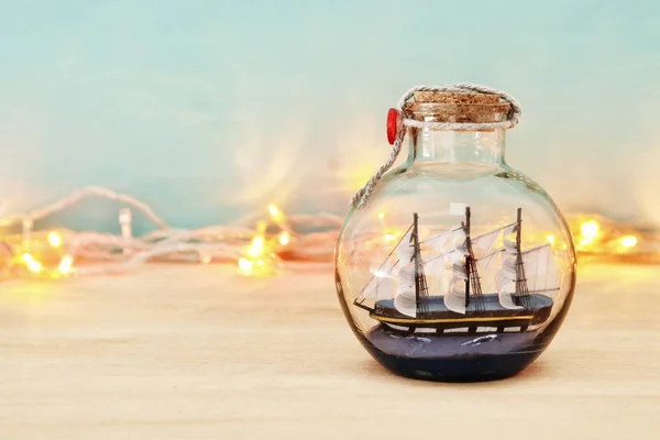 Námořních koncept obrázek s plachetnice v láhvi a zlatý věnec světel nad dřevěný stůl. Selektivní fokus. — Stock fotografie