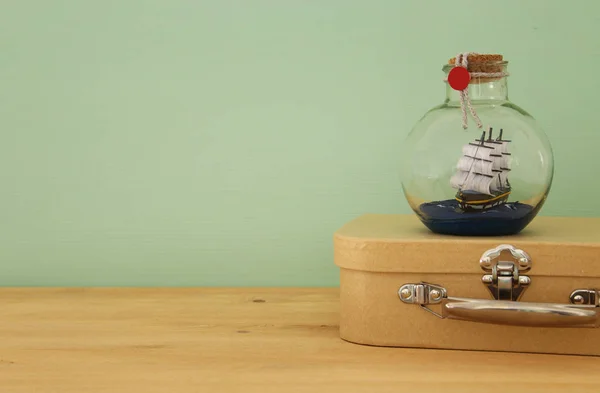 Морское концептуальное изображение с парусной лодкой в бутылке и старым чемоданом над деревянным столом. Селективный фокус . — стоковое фото