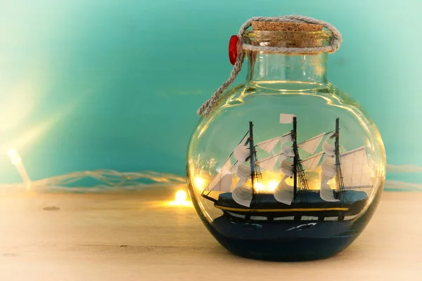 Морское концептуальное изображение с парусником в бутылке и золотыми гирляндами над деревянным столом. Селективный фокус — стоковое фото