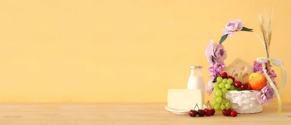 Bild von Früchten und Käse in dekorativem Korb mit Blumen über Holztisch. Symbole des jüdischen Feiertags - shavuot. — Stockfoto