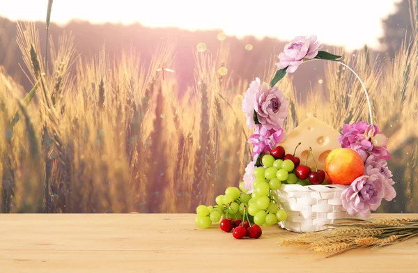 Bild von Früchten und Käse in dekorativem Korb mit Blumen über Holztisch. Symbole des jüdischen Feiertags - shavuot. — Stockfoto