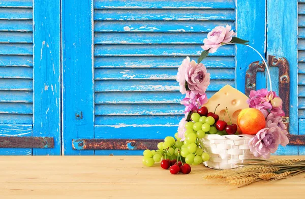 Obraz z owoców i sera w dekoracyjny kosz z kwiatami na drewnianym stole. Symbole żydowskiego święta - Szawuot. — Zdjęcie stockowe