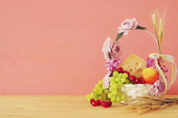 Image of fruits and cheese in decorative basket with flowers over wooden table. Symbols of jewish holiday - Shavuot. — Stock Photo, Image