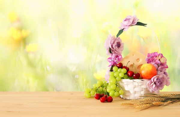 Obraz z owoców i sera w dekoracyjny kosz z kwiatami na drewnianym stole. Symbole żydowskiego święta - Szawuot. — Zdjęcie stockowe