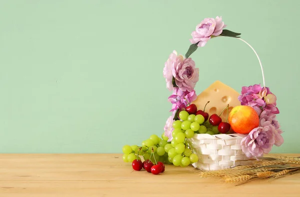 Imagem de frutas e queijo em cesta decorativa com flores sobre mesa de madeira. Símbolos de férias judaicas - Shavuot . — Fotografia de Stock