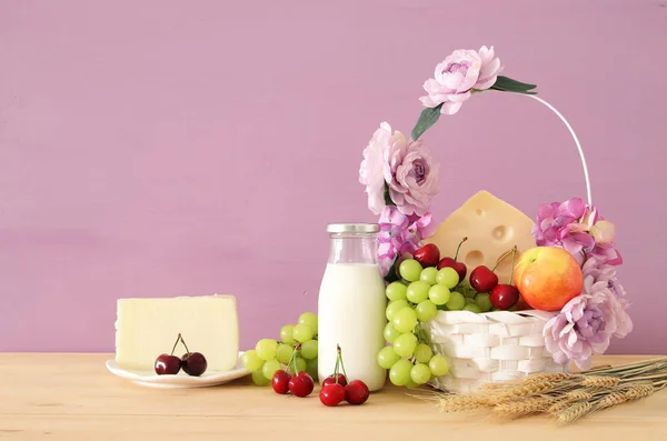 Afbeelding van fruit en kaas in de decoratieve mand met bloemen over houten tafel. Symbolen van Joodse vakantie - Sjavoeot (Wekenfeest). — Stockfoto