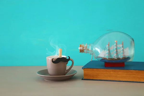 Bild av kopp kaffe, Gammal bok och båt i flaskan över träbord. Fars dag-konceptet. — Stockfoto
