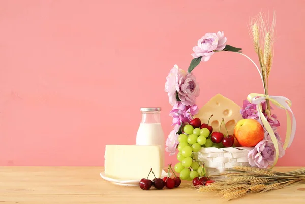 Imagen de frutas y queso en cesta decorativa con flores sobre mesa de madera. Símbolos de la fiesta judía - Shavuot . — Foto de Stock