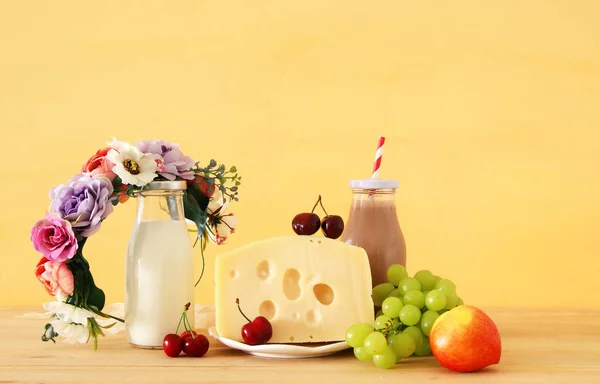 Bild av frukt och ost i dekorativ korg med blommor över träbord. Symboler för judiska semester - Shavuot. — Stockfoto